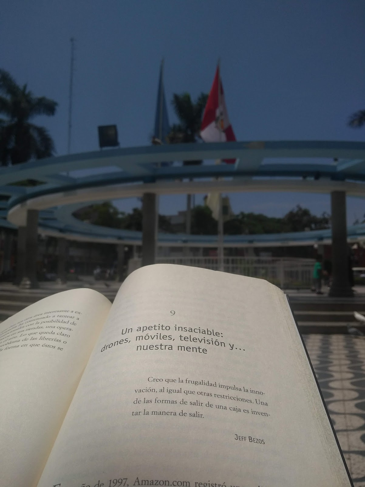 Leyendo a Jeff Bezos en una plaza de Lima, con la bandera del Perú de fondo.